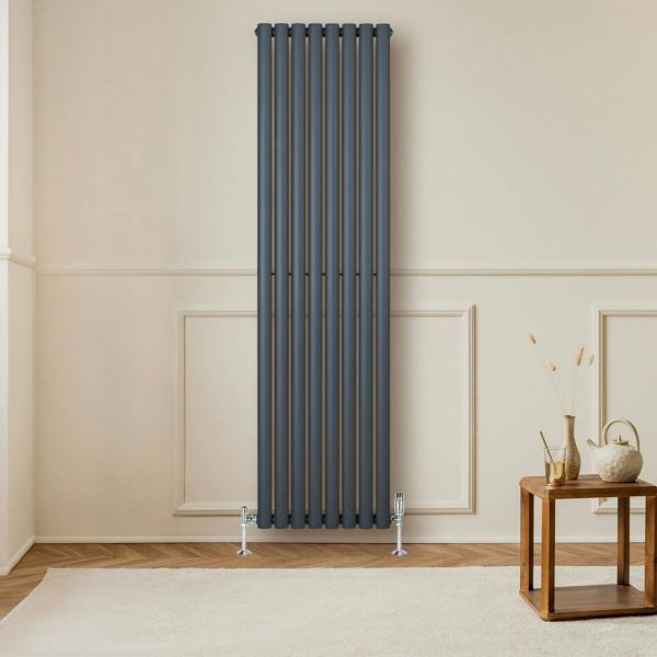 Sleek anthracite grey oval single column radiator mounted on a wall, complemented by stylish valves and a wooden side table