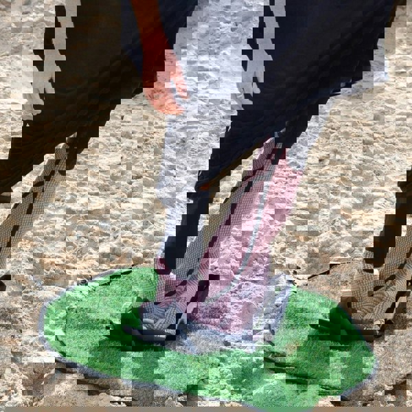 Person standing on a green mat with sand in the background