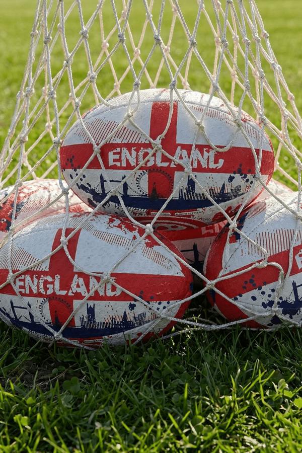 White and red Optimum England rugby balls with St George's cross and ENGLAND print in a net bag on grass - Optimum
