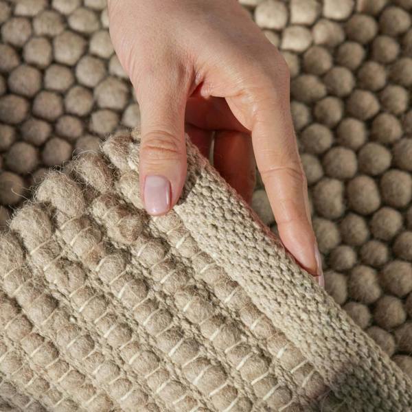 Hand holding a textured beige rug against a matching hexagonal patterned background