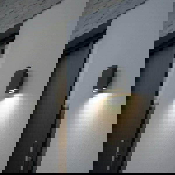 black outdoor LED wall downlight mounted on a white exterior wall next to the front door of a home 