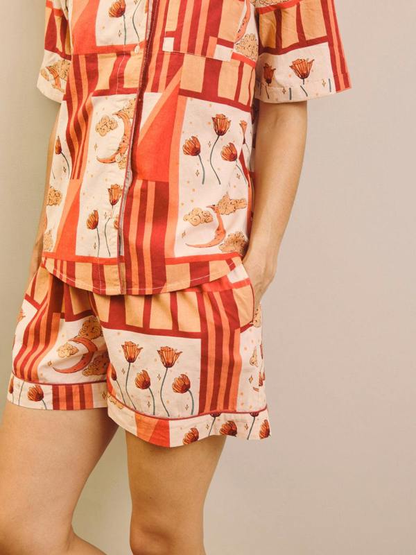 Woman wearing a rust and cream patch work patterned pyjama set against a plain wall. Detail