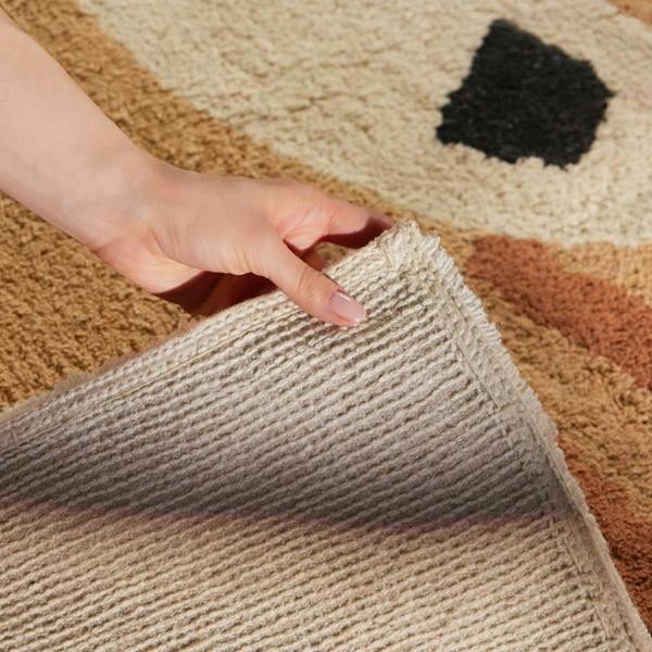 Hand touching a textured beige rug with a patterned background