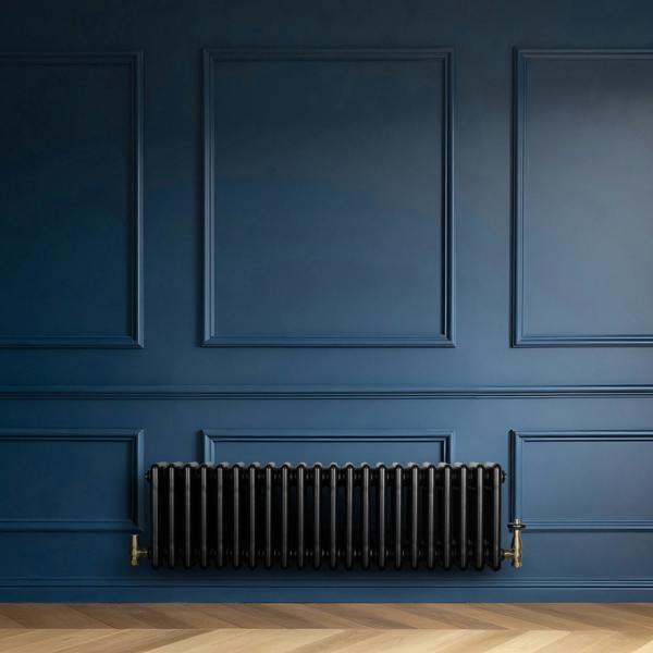 Traditional black 4 column radiator with brass valves, mounted on a deep blue wall, complementing a herringbone wood floor