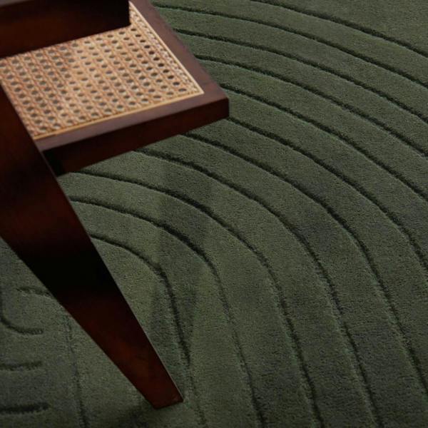 Green textured rug with a wooden stool featuring a woven seat.