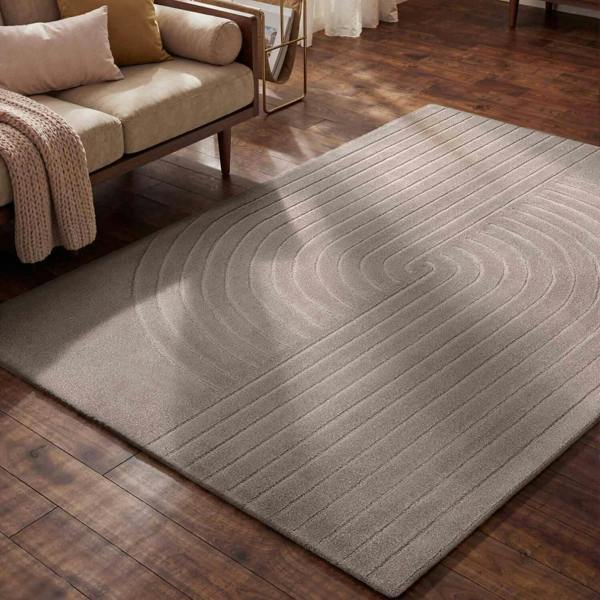Gray area rug on a wooden floor with a beige sofa in the background