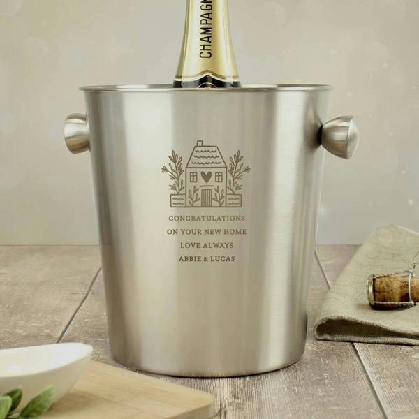Brushed stainless steel ice bucket engraved with a house illustration and custom text holding a champagne bottle on a wooden table
