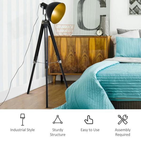 Tripod floor lamp with black frame and gold spotlight shade near a bed