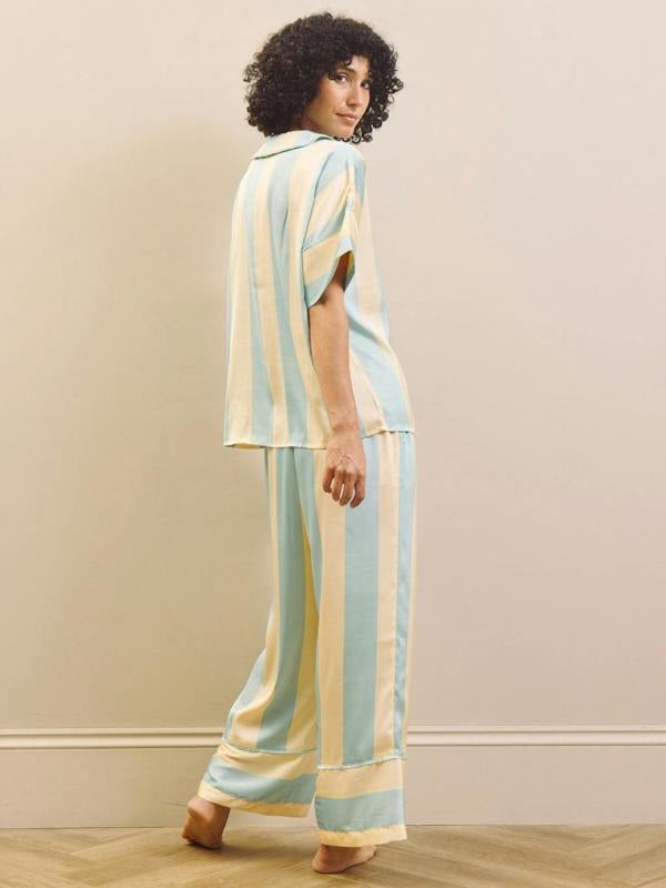 Woman wearing a striped pyhama standing against a plain wall.
