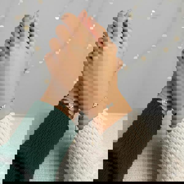 Two hands wearing delicate bracelets against a soft background