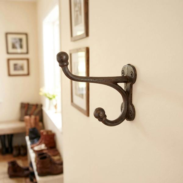 Heavy-duty antique cast iron hall stand hook on a light-colored wall in a rustic entryway, with shoes and bags in the background.