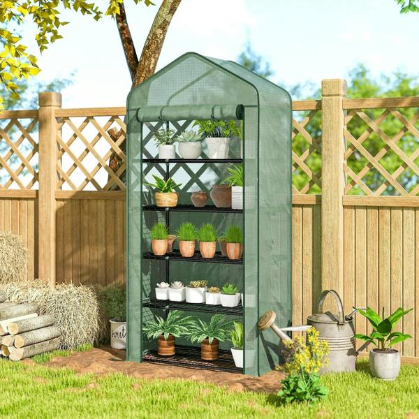 Green mini greenhouse with clear PE cover and five wire shelves in a backyard corner.