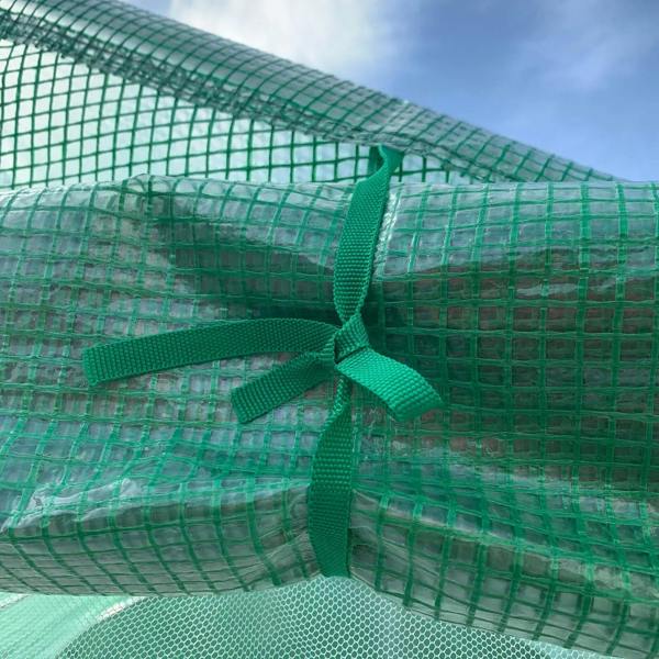 Green mesh greenhouse cover secured with fabric ties on the roof