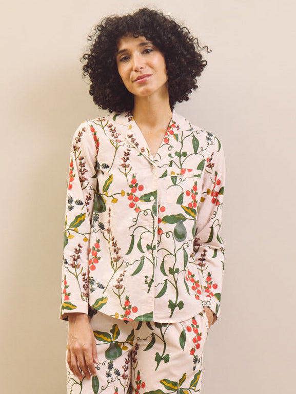 Woman wearing a pear & floral pyjama set against a plain wall.