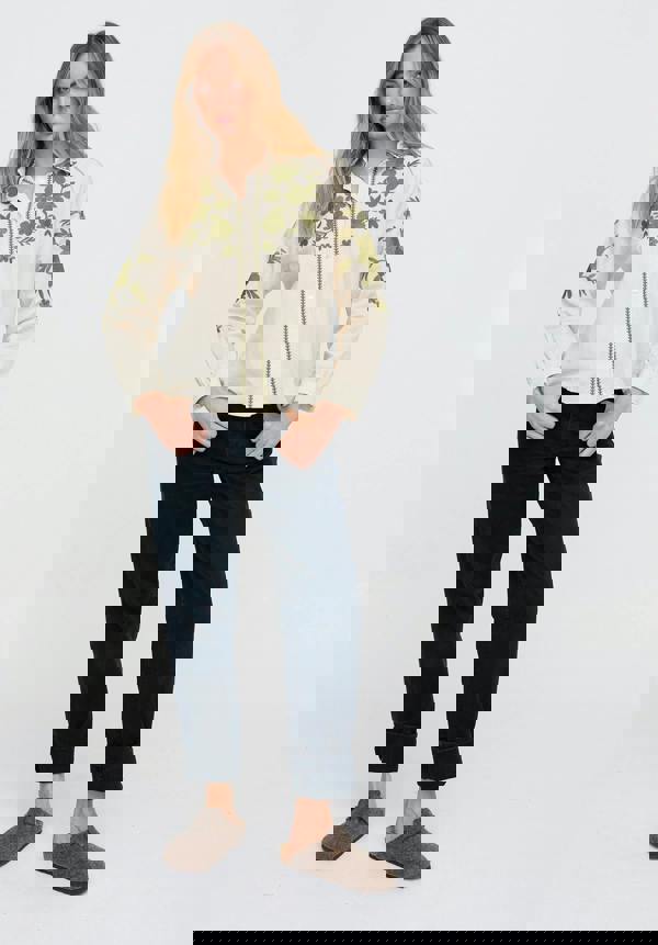 Woman wearing a cream floral blouse and dark pants on a white background