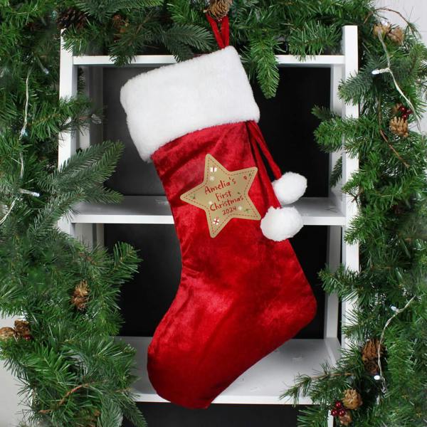 A red velvet-style Christmas stocking with a white fur cuff and a star reading Amelia's First Christmas 2024.