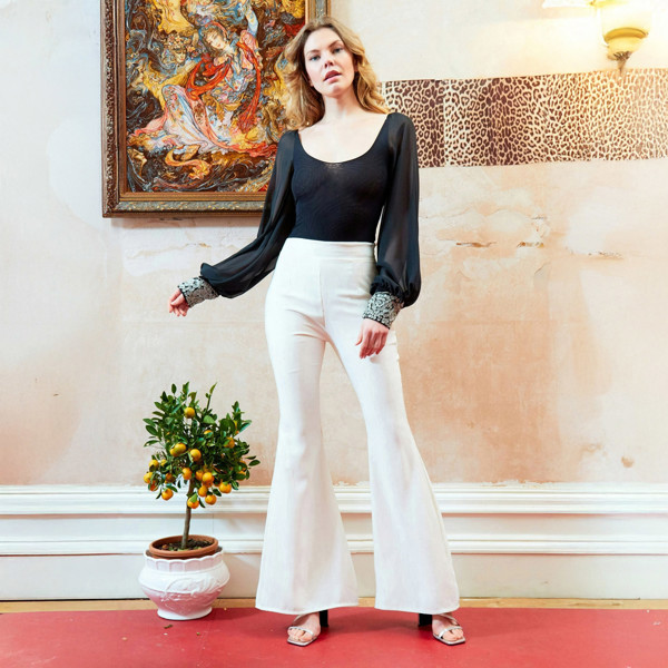 A woman is standing in a room wearing white pants and a Sarvin Black Mesh Bodysuit Long Sleeve.