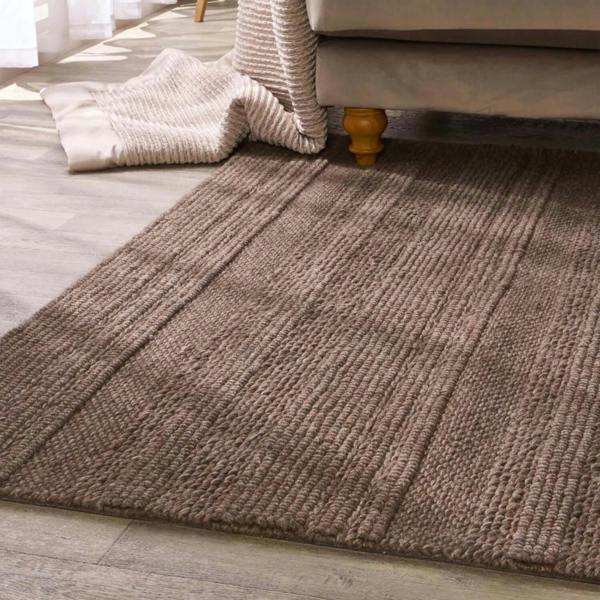 Brown textured rug on a wooden floor with a beige sofa and white curtains in the background.