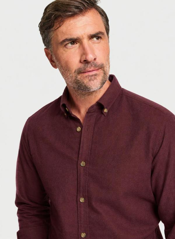 A close-up shot of a man wearing a maroon long-sleeve button-down shirt against a light gray background.