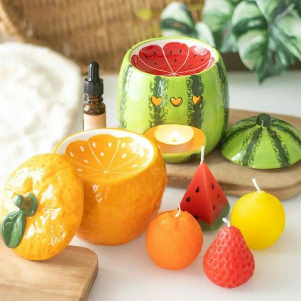 Fruit-shaped candles with wicks: orange, lemon, strawberry, watermelon slice on tray.