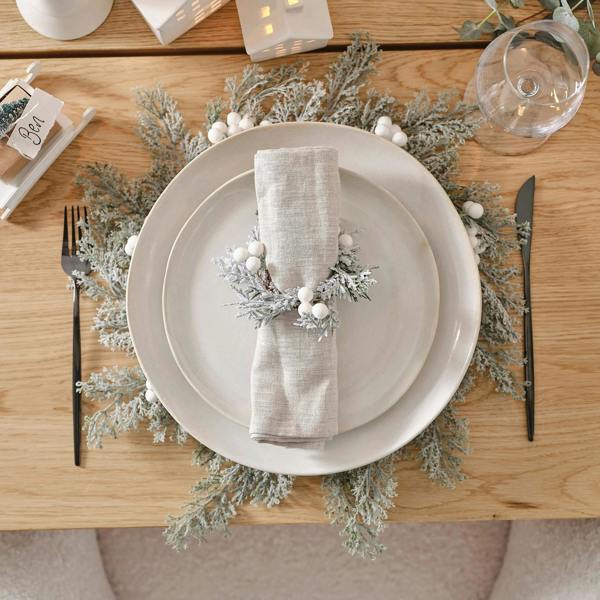 Set of Four Snowy Foliage & White Berry Place Mats on a wooden table with white plates and neutral linens.