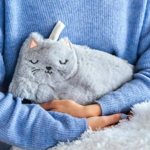 Close-up of a person in a blue ribbed jumper hugging a plush grey faux-fur cat hot water bottle.