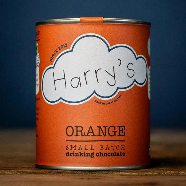 Recyclable vibrant orange tin of Harry's Small Batch Orange Drinking Chocolate resting on a rustic wooden surface.