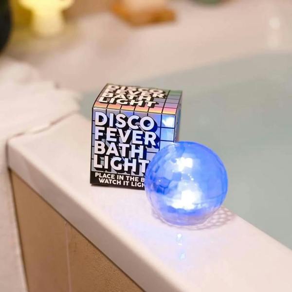 A glowing blue Disco Fever Bath Light next to its packaging box on the edge of a white bathtub.