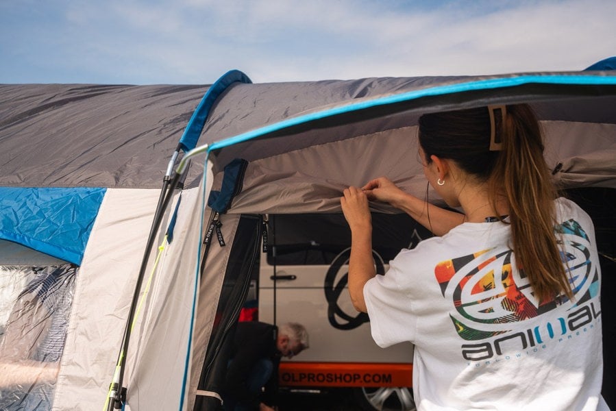 A camper rolling up the door & fly mesh on the side door of the Cocoon V2 Poled Campervan Awning by OLPRO