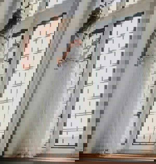 girl in a white dress standing by a large window