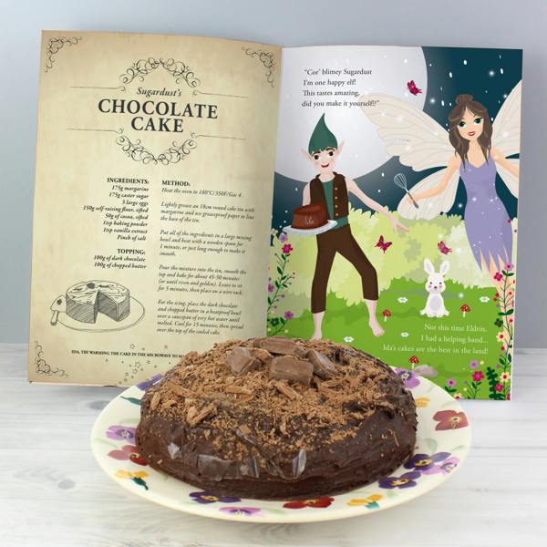 Open view of the Personalised Fairy Baking Adventure storybook showing Sugardust's Chocolate Cake recipe next to Eldrin the Elf holding a cake with Ida written on it, displayed behind a baked chocolate cake