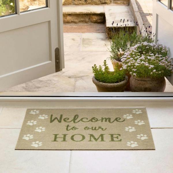 Doormat with 'Welcome to our Home' text and paw prints on a tiled floor, leading to an outdoor area.