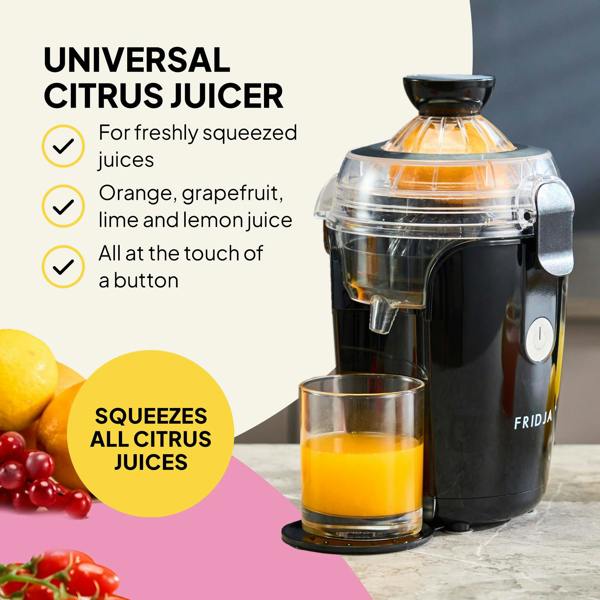 The Fridja f800 Automatic Citrus Juicer, in black, sits on a counter beside a glass of fresh juice, lemons, and grapes. It offers vitamin C-rich drinks from various citrus fruits with just the touch of a button.