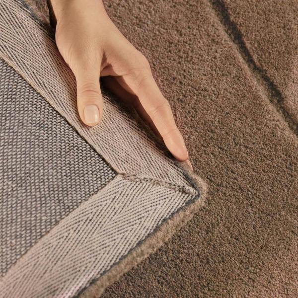 Close-up of a hand touching the edge of two carpets with a visible seam.