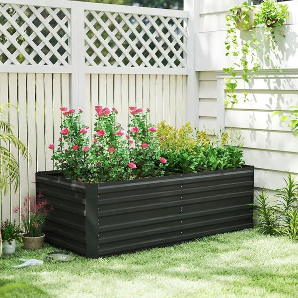 Black raised garden bed planter with pink flowers and green plants against a lattice fence