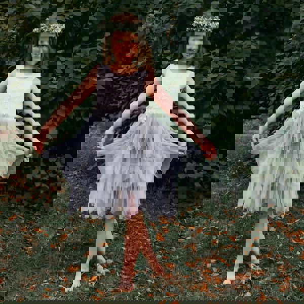 Young girl in a white and gray dress with a floral headband standing outdoors.