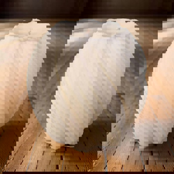 An unscented natural wax candle with a lit flame, placed in a metal holder with a textured white wax surface.