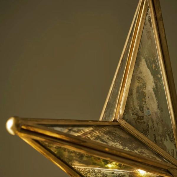 Cotswold hand-hammered steel star tree topper with an antique brass finish securely styling the top of a traditional lit green Christmas tree.