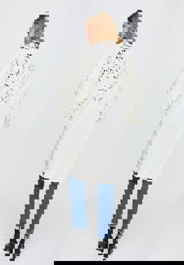 Person wearing a white coat with decorative patterns on a plain background