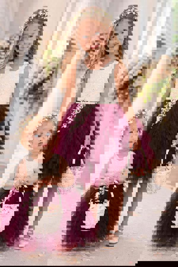 Two young girls in matching dresses with floral headbands and baskets indoors.