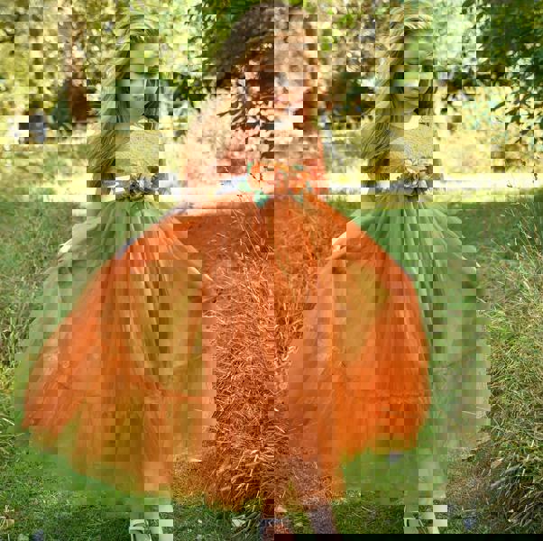 Young girl in an orange dress standing in a grassy field with trees in the background