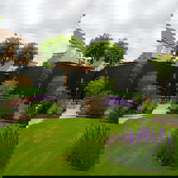 Backyard garden with a patio area, trees, and various plants on a cloudy day. With a feature black slat clad fence