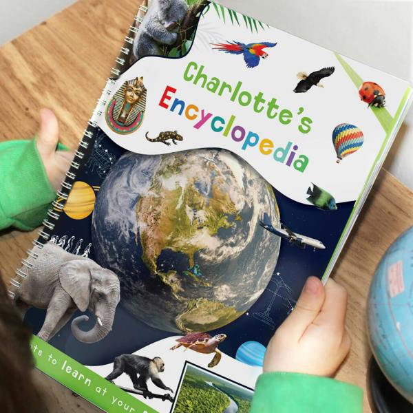 A child holding an open spiral-bound Personalised Childrens Encyclopaedia featuring Charlotte on the cover with colourful lettering and a globe design.