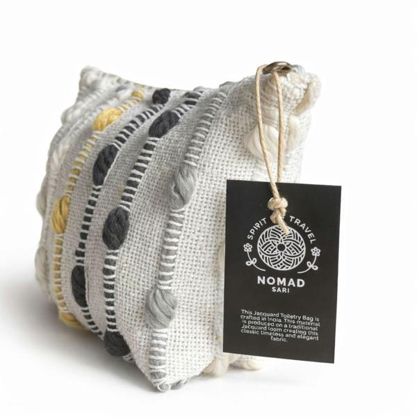 Nomad Sari jacquard toiletry bag close-up with fabric stripes and black pom-pom trim tag.