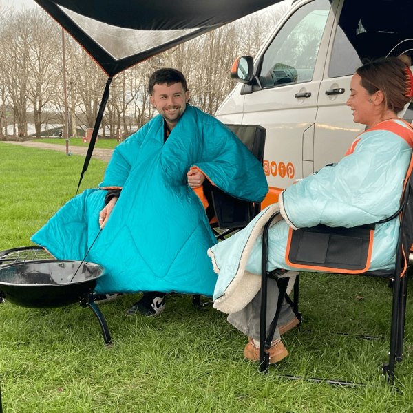 a couple in camping chairs relax in comfort with their insulated OLPRO Blanko Outdoor Blanket.