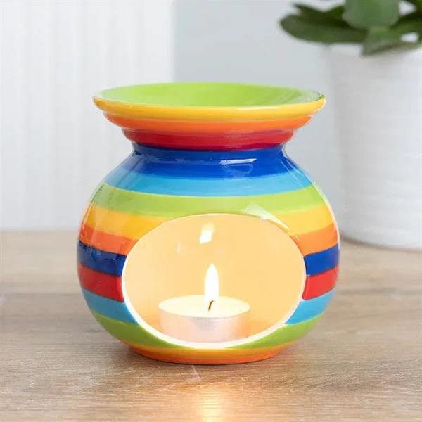Rainbow striped oil burner with lit tealight, glossy ceramic jar on tabletop