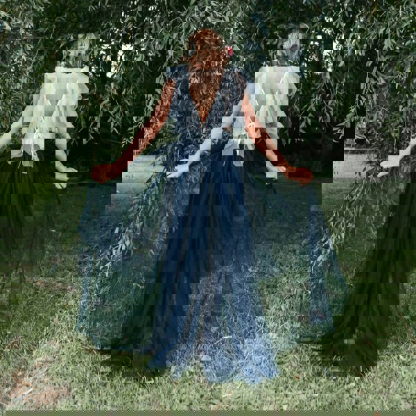 Girl in a blue and white dress standing in a grassy area with trees.