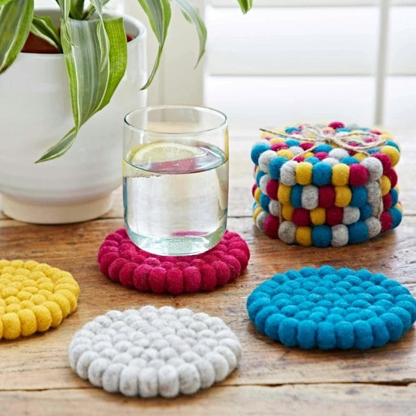 A Set of 4 Handmade Felt Ball Coasters with a glass of water next to them.