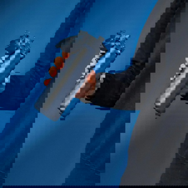 A person holds a blue water bottle with a flip-top lid against a solid blue background wearing a dark sweatshirt.