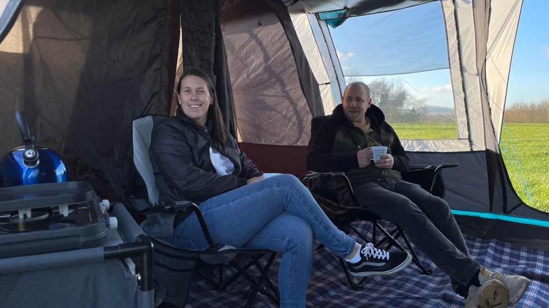 An image of two adults sat on the Henwick Padded Folding Camp Chairs - Green & Black from OLPRO inside of a tent.